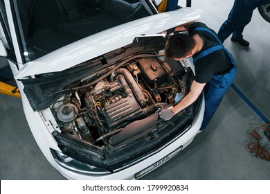 Under the hood. Man in work uniform repairs white automobile indoors. Conception of automobile service. - Powered by Shutterstock