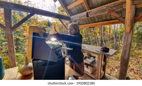 Under The Not Yet Finished Roof Of A Little Shack In The Woods Ready To Become A Mini House, A Young Woman Is At The Kitchen Stove, Cooking Something.