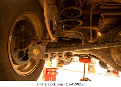 Under old car closeup rear wheel axle suspension and exhaust chamber silencer muffler dirty fix repair in garage. - Shutterstock ID 1824538250