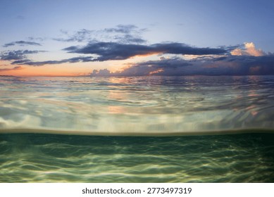 An under over split view of an idyllic clear water sandy beach captured on sunrise.