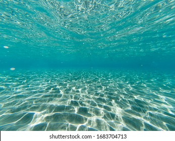 Under Water Photo Of Sandy Seabed With Sunlight Trough Water Surface.