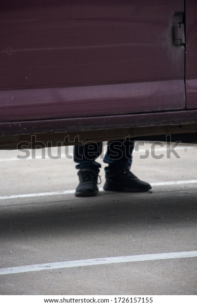 undercarriage of purple vehicle in a parking\
lot with feet and legs in bokeh effect\
black