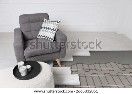 Underfloor heating system installed in room with armchair and pouf. Pipes seen under laminate
