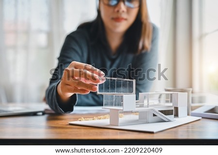 Undergraduate architecture students work on models of the modern box glass house. Holding the part of the model while thinking about concepts of building and construction. Focusing on her hand.