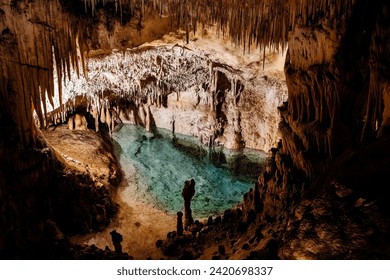 "Underground cave, stalactites, stalagmites, clear blue water pool, illuminated."