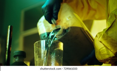 In the Underground Drug Laboratory Clandestine Chemist Wearing Protective Mask and Coverall Mixes Chemicals. He Pours Liquid From Canister into Bowl to Make New Batch of Synthetic Narcotics.