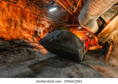 An underground loading machine carries a full bucket of ore. Special low-profile equipment for underground work.