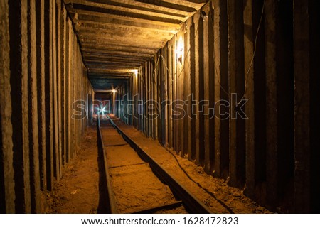 Underground square tunnel with rails for minecart and warm tungsten lighting and flashlight in the end. 