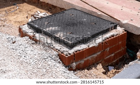 Underground utility access cover installed in a brick inspection chamber during road construction. Infrastructure work with concrete, gravel and excavation.