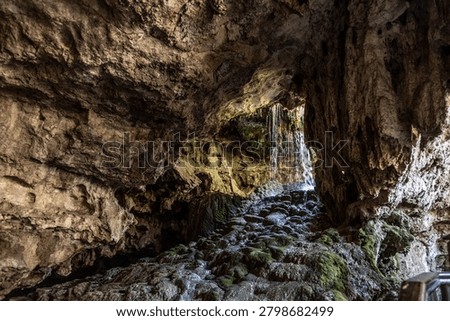 Underground waterfall cascade inside limestone cave tunnel with green moss rock. Kaklik cavern interior with water stream, geological landmark under day light, Denizli, Anatolia, Turkey.