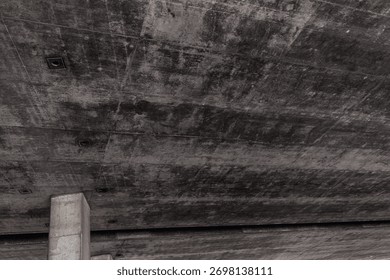 The underside of a modern elevated highway structure or concrete bridge, dark, textured surface, possibly due to aging or moisture, the structure is supported by concrete pillars
