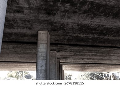 The underside of a modern elevated highway structure or concrete bridge, dark, textured surface, possibly due to aging or moisture, the structure is supported by concrete pillars