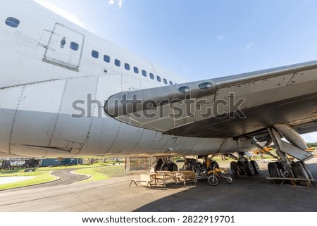 Underside view of a large commercial airplane fuselage and wing parked outdoors on a sunny day.