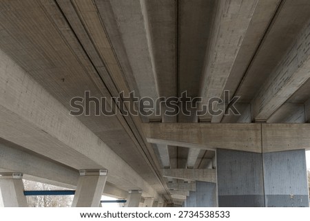Underside view of a massive modern concrete bridge showing parallel support beams and robust columns