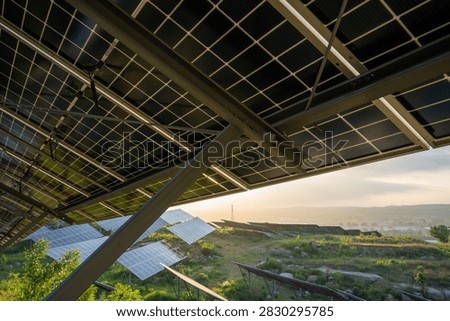 Underside view of solar panels mounted on a structure at an outdoor renewable energy generation site.