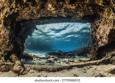 An underwater cave frames a view of the ocean's depths, showcasing the vibrant marine environment and the interplay of light and water.