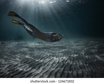 Underwater Full Length Portrait Of A Woman Snorkeling In Tropical Sea Over Sandy Bottom