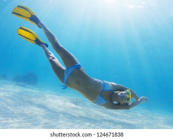 Underwater Full Length Portrait Of A Woman Snorkeling In Tropical Sea Over Sandy Bottom