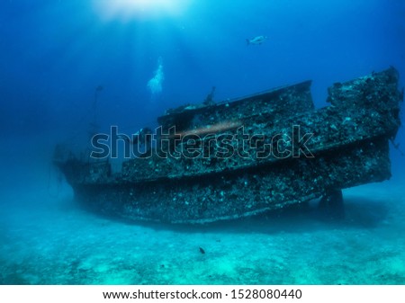 Underwater panorama of a scuba diver with a torch exploring a sunken shipwreck at the Maldives islands, Indian Ocean