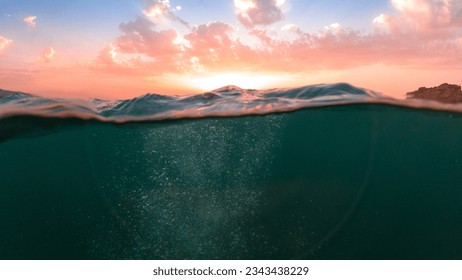 Underwater part and sunset skylight splitted by waterline, underwater bubbles. Beautiful clouds and bright sun over sea water, Real image very suitable for backgrounds in Mediterranean sea, undersea.