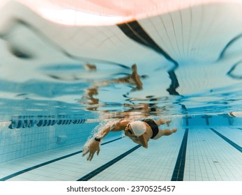 Underwater photo of an adult man with an amputated arm swimming in an indoor pool. The athlete is crawling with only one arm. Disabled swimmers, athletes with an amputated arm. - Powered by Shutterstock