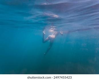 Underwater photo, a girl swims near a shark net in the sea.  - Powered by Shutterstock