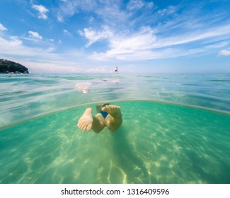Underwater photo of woman swimming in ocean. View from the back. Split view cross section of sea water and blue sky. 