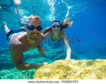 Underwater photo of a young tourist love couple swimming in the turquoise sea under the surface near coral reef while holding hands together for summer vacation.