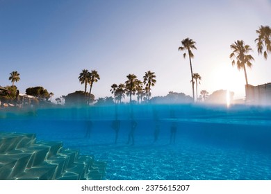 Underwater photography of people standing in pool with copy space. Beach resort vacation by sea. Winter or summer seaside resort holiday. Over-under underwater photography.