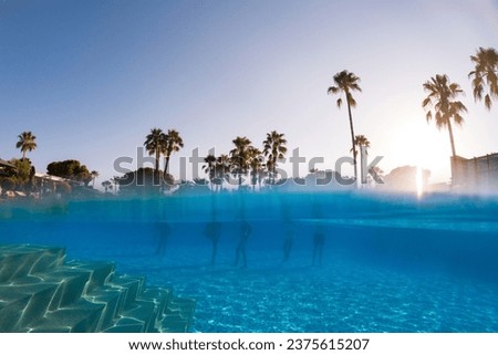 Underwater photography of people standing in pool with copy space. Beach resort vacation by sea. Winter or summer seaside resort holiday. Over-under underwater photography.