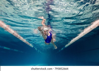 underwater picture of female swimmer in swimming suit and goggles training in swimming pool