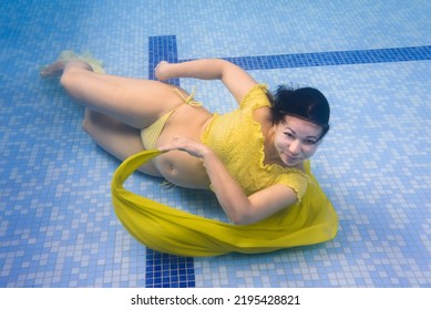 Underwater Pregnant Woman Wearing Dress In Deep Pool. Girl Swim, Dive In Swimming Pool. Aqua Fitness Healthcare Classes For Pregnancy. Aquatic Therapy Workout. Safest Most Efficient Form Of Exercises.