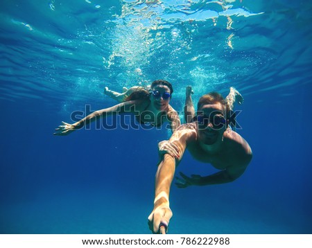 Underwater selfie with a stick of a happy handsome love couple swimming in the turquoise sea under the surface for summer vacation.
