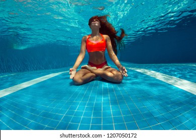 Underwater shoot of a relaxed smiling woman flying in a swimming pool in lotus position
