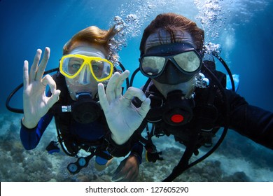 Underwater shoot of a young couple diving with scuba in a tropical sea and showing ok signal