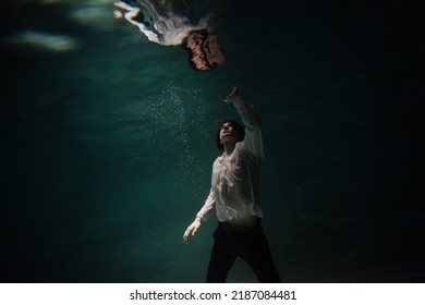 underwater shooting with contrasting light, a guy is swimming underwater, pulling his hand to his reflection in the surface of the water. Subconsciousness and self-reflection, concept - Shutterstock ID 2187084481