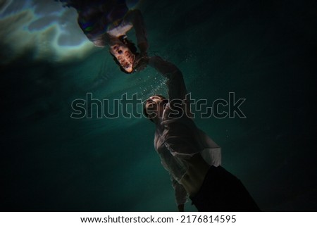 underwater shooting with contrasting light, a guy is swimming underwater, pulling his hand to his reflection in the surface of the water. Subconsciousness and self-reflection, concept