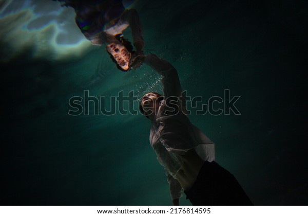 underwater\
shooting with contrasting light, a guy is swimming underwater,\
pulling his hand to his reflection in the surface of the water.\
Subconsciousness and self-reflection,\
concept
