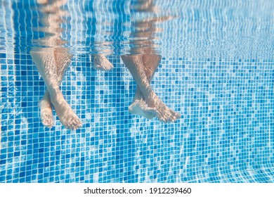 Underwater Shot Of Couples Legs As They Sit On Edge Of Swimming Pool On Vacation - Powered by Shutterstock