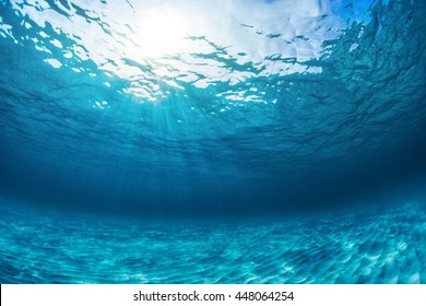 Underwater shot of an infinite sandy sea bottom with clear blue water and waves on its surface - Shutterstock ID 448064254