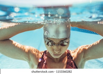 Underwater Shot Of Woman Inside Swimming Pool. Female Swimmer In Swim Cap And Goggles Inside Pool.