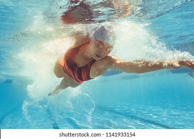 Underwater shot of woman swimming the front crawl in sports pool. Fit female athlete practising in swimming pool.