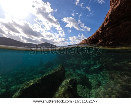 Unbekannter Jugendlicher in Neoprenanzug und Schnorchel im klaren Wasser mit felsigen Klippen von Menorca, Spanien, geteilter Blick über und unter der Wasseroberfläche