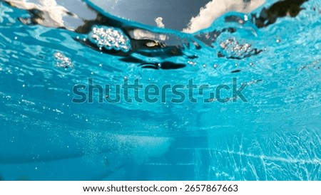 Underwater view of a backyard pool with steps, bubbles, and shimmering reflections, showing the surface tension and sky clouds from below the water 