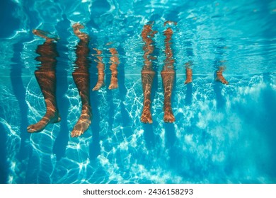 Underwater view of diverse people's legs, adults and kids, suspended in a clear blue sunny swimming pool dangling around - Powered by Shutterstock