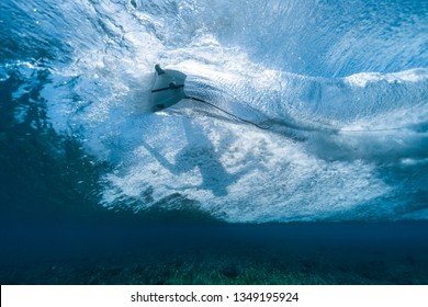 Underwater view of the surfer riding the crystal clear ocean wave and making sharp turn
