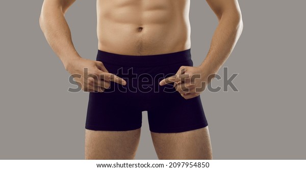 Underwear.Man fingers pointing at black\
classic shorts boxers in which he is dressed, isolated on gray\
background. Close up of underpants on man with perfect fit body.\
Advertising men\'s\
briefs.Banner