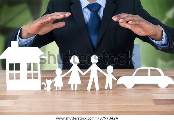 underwriter protecting family in paper with\
his hands against office buildings with\
graphs