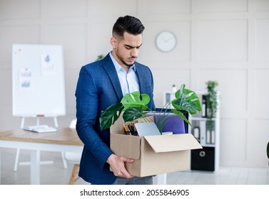 Unemployed Arab guy in formal wear holding personal belongings, feeling depressed after losing his job. Upset Eastern man with cardboard box of things leaving office after being fired