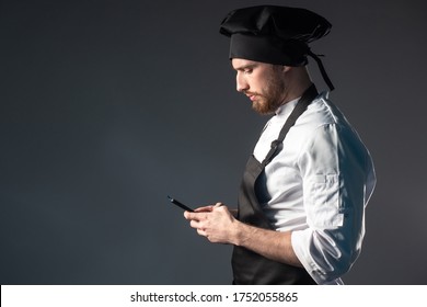 An Unemployed Chef. A Man Is Looking For A Job In A Restaurant. Vacancies In The Field Of Public Catering. Cook Jobs. A Chef In A Black Uniform With A Mobile Phone In His Hands. 